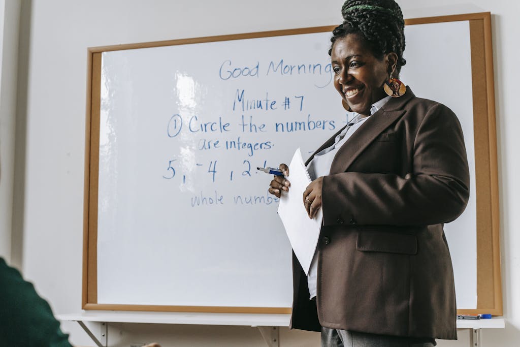 crop smiling african american female teacher standing near whiteboard with papers in hands during math lesson 5905456